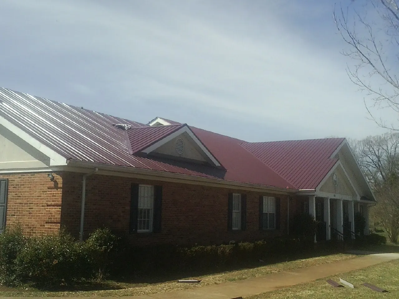 Red metal roof with gabled entries on a long brick building, from a Hail Damage Roof Repair job in Mine Hill