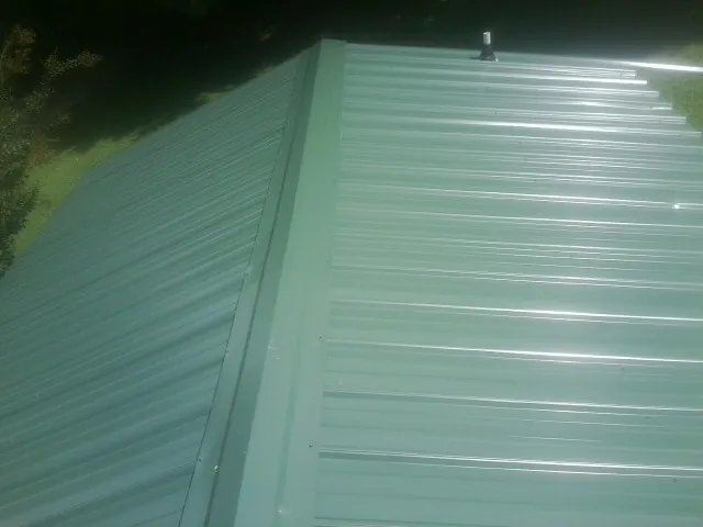 New green metal panels meeting at the ridge of a roof — Flat Roof Repair work by our crew in Mine Hill