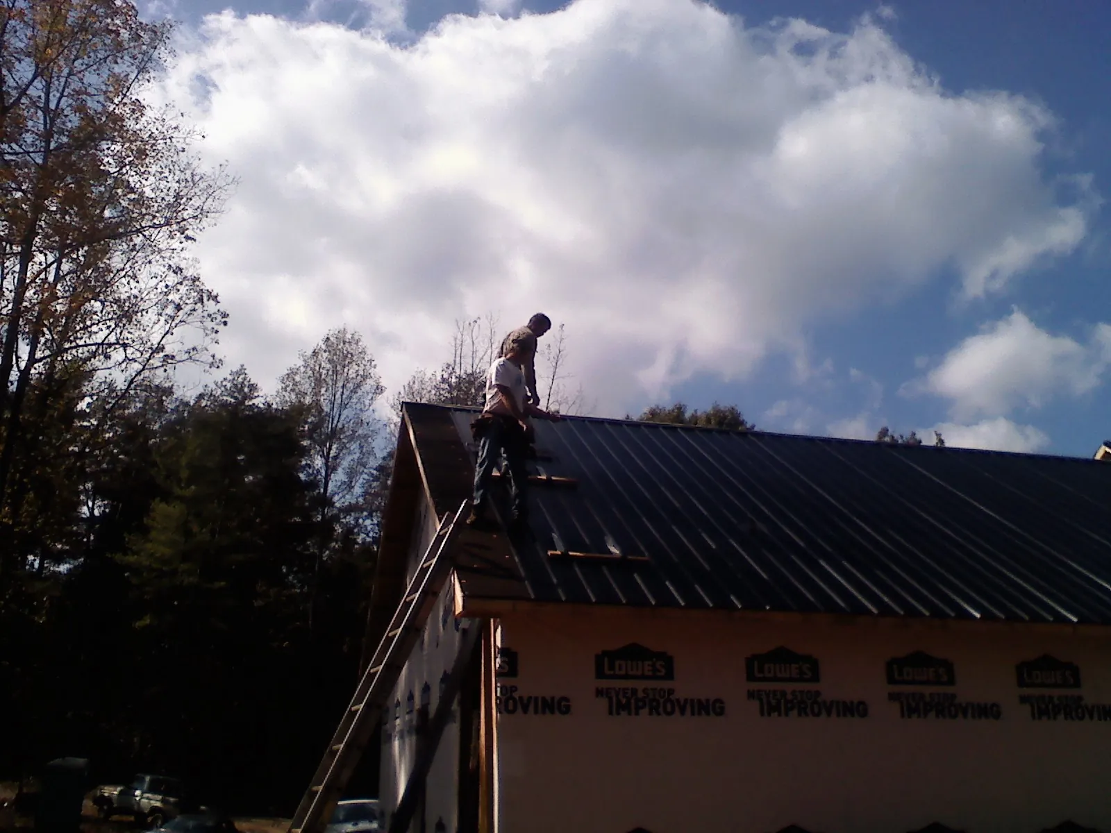 Roofer fastening dark metal panels high against a cloudy sky, from a Roof Inspection job in Mine Hill