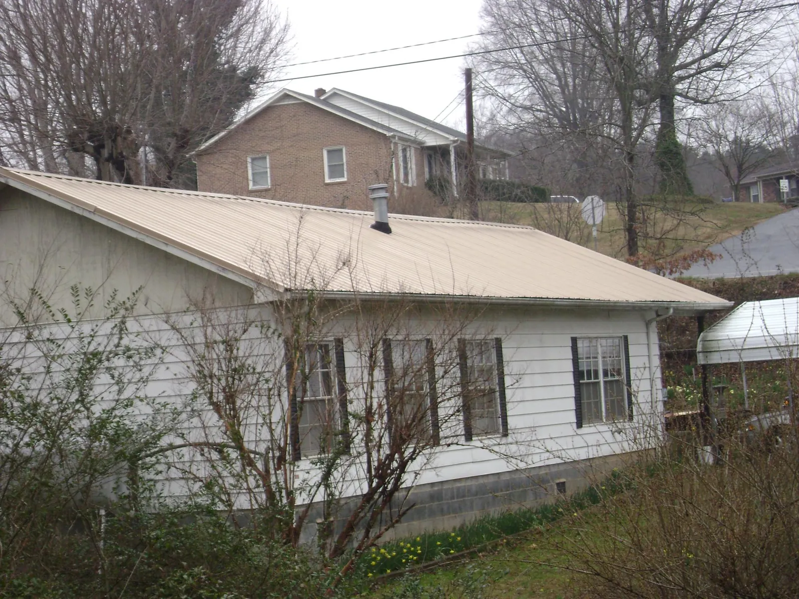 Tan metal roof on a white sided house set into a hillside — Commercial Roofing by Roofing Brothers in Mine Hill